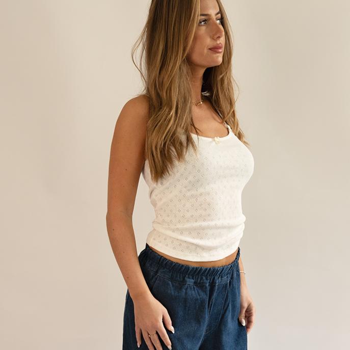 Woman wearing a white top and blue pants against a plain background