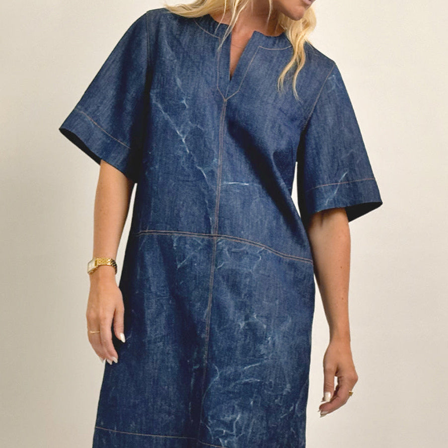 Woman wearing a blue denim dress against a beige background