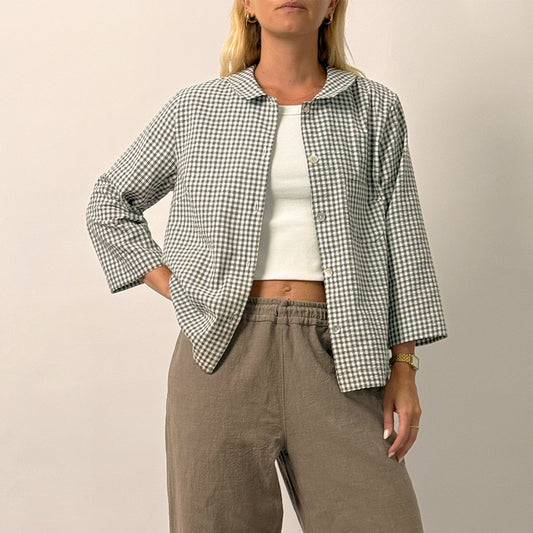 Woman wearing a checkered jacket, white top, and brown pants on a plain background