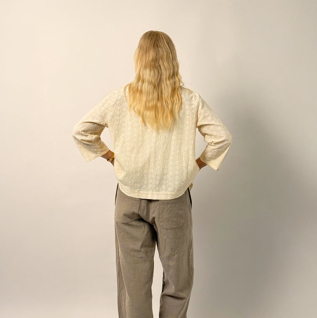 Person wearing a beige shirt and gray pants against a plain background