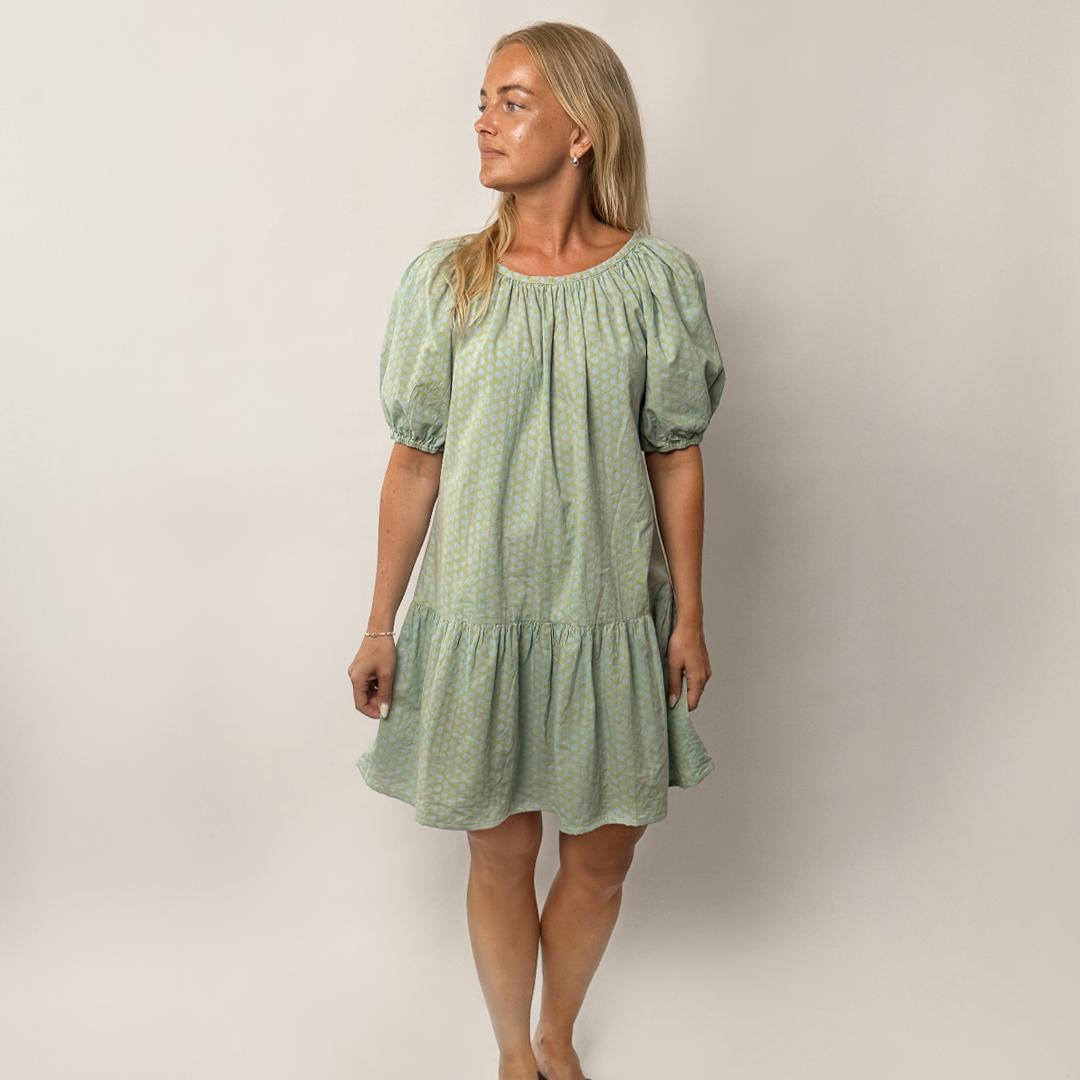 Woman wearing a green dress with puff sleeves against a plain background