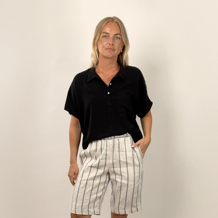 Person wearing a black shirt and striped shorts on a plain background