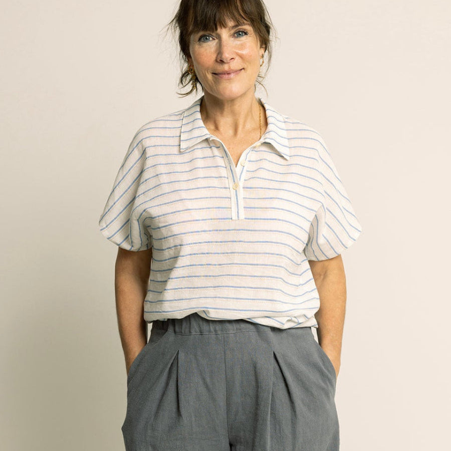 Woman wearing a striped shirt and gray wide-leg pants against a plain background