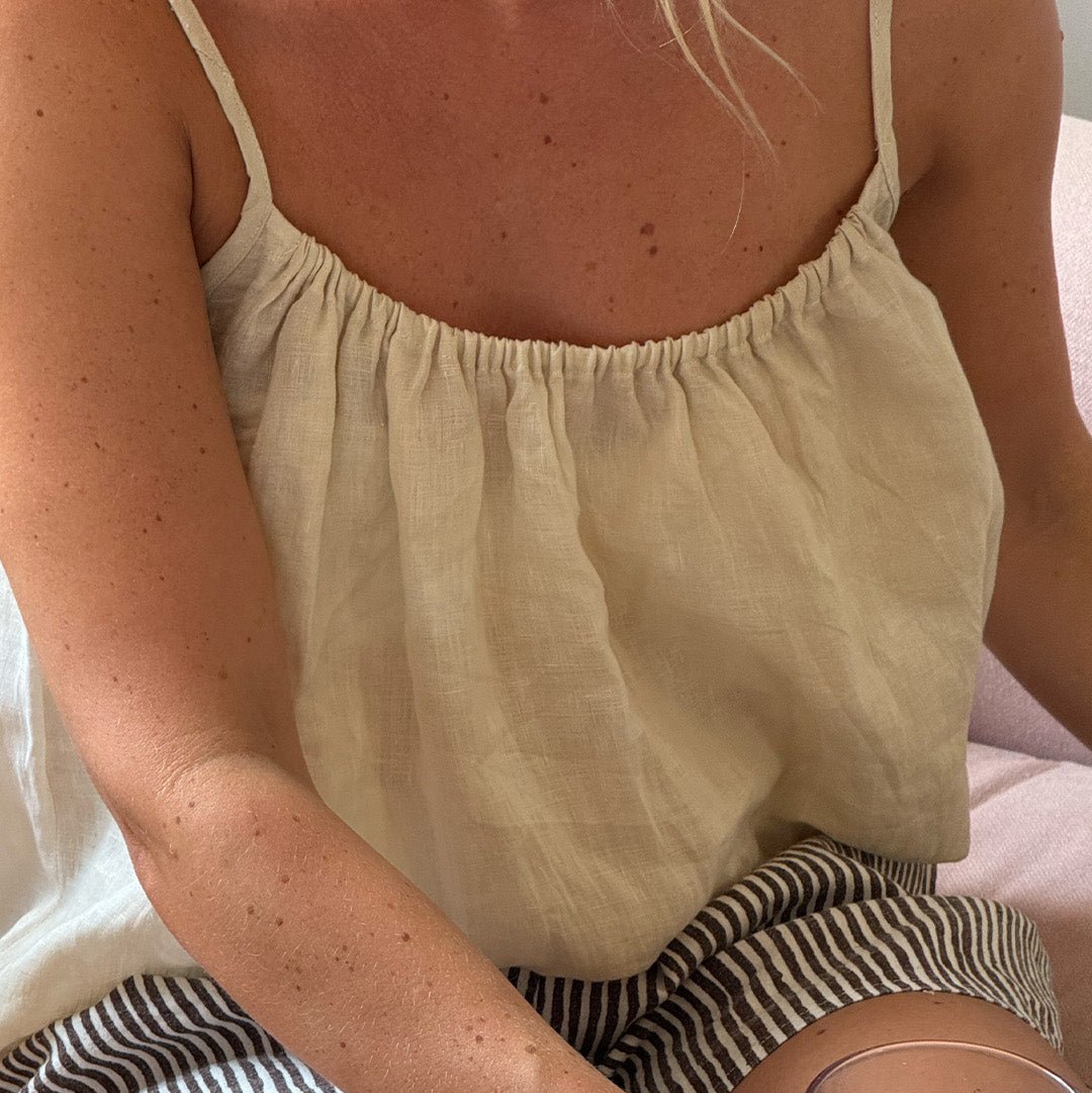 Person wearing a light-colored top and striped shorts, holding a glass of red wine.