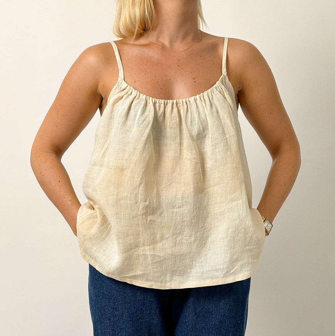 Woman wearing a beige tank top and blue pants against a plain background