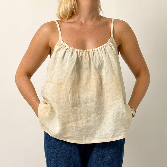 Woman wearing a beige tank top and blue pants against a plain background
