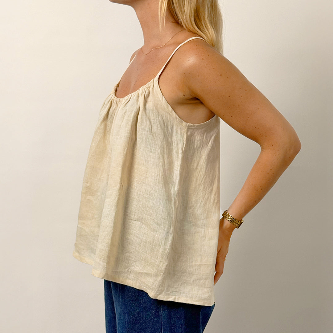 Woman wearing a beige sleeveless top and blue pants against a plain background