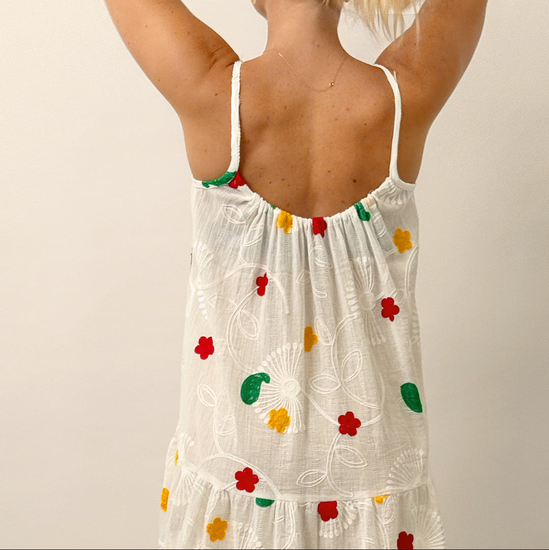 Woman wearing a white dress with colorful floral patterns on a plain background