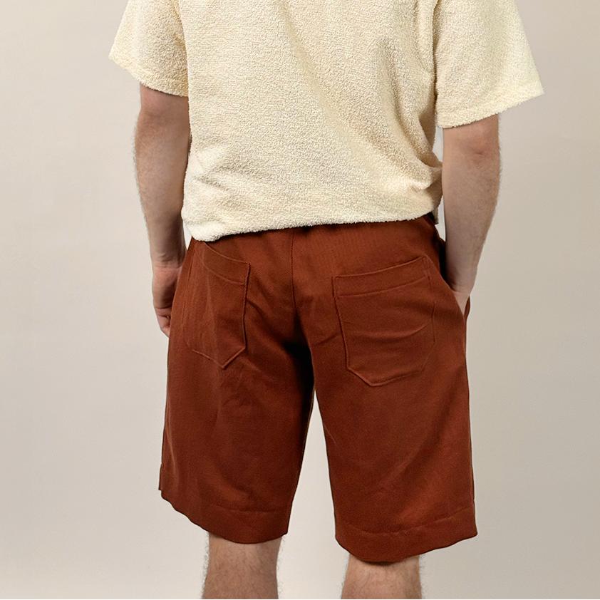 Man wearing a beige shirt and rust-colored shorts against a plain background