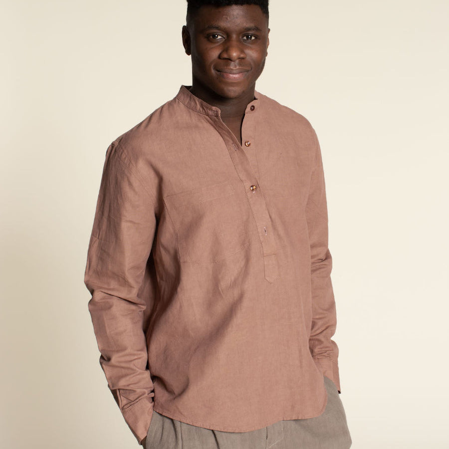 Man wearing a brown long-sleeve shirt and beige pants against a beige background