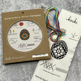 Kraft board packaging with cream cotton stitch sampler featuring a pysanky egg decorated in star and vines and hank of cotton embroidery floss in jewel tones