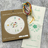 Kraft board packaging with cream cotton stitch sampler featuring flowers and leaves and hank of cotton embroidery floss in spring color palette